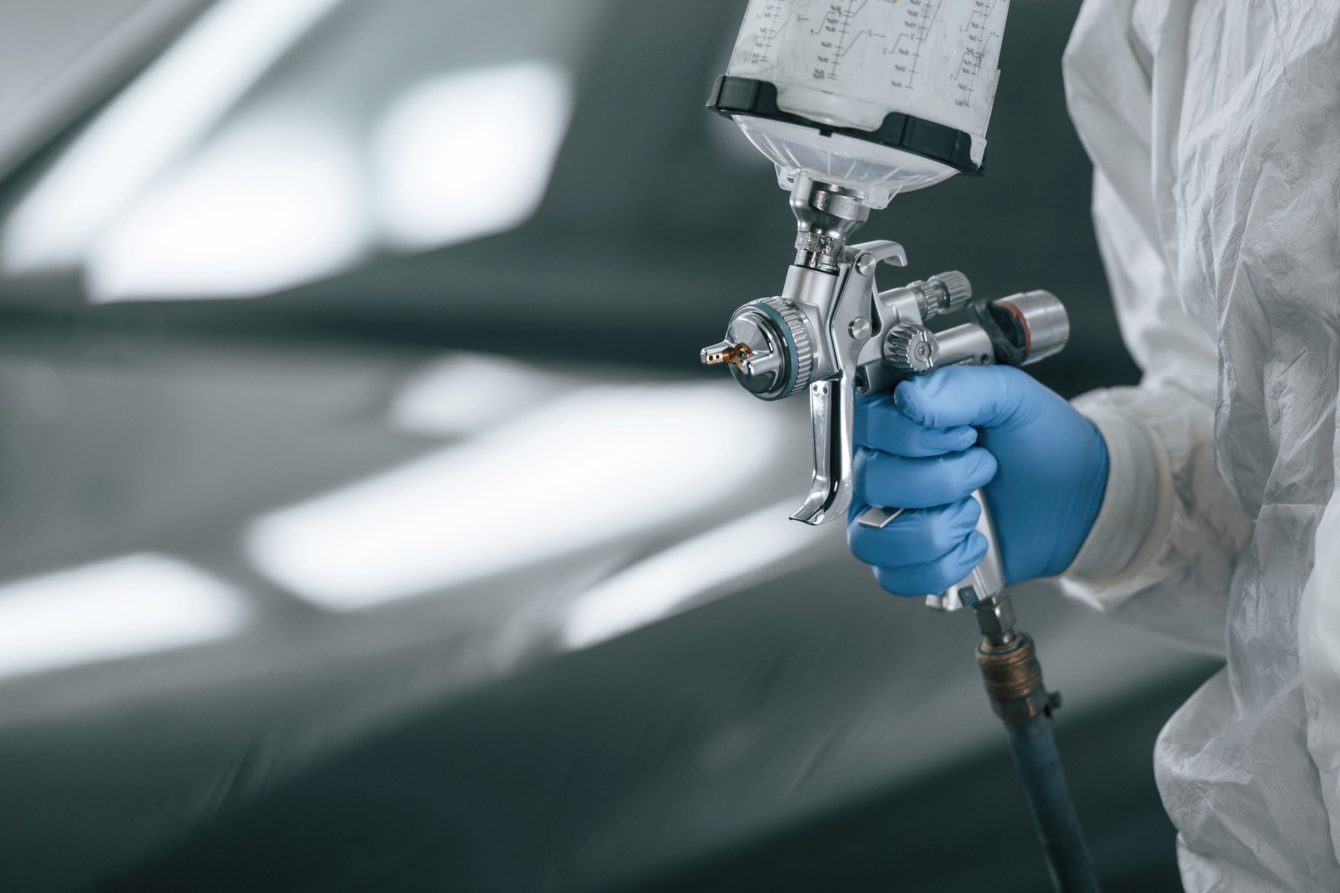Focused close up view. Man is holding spray gun for painting a car